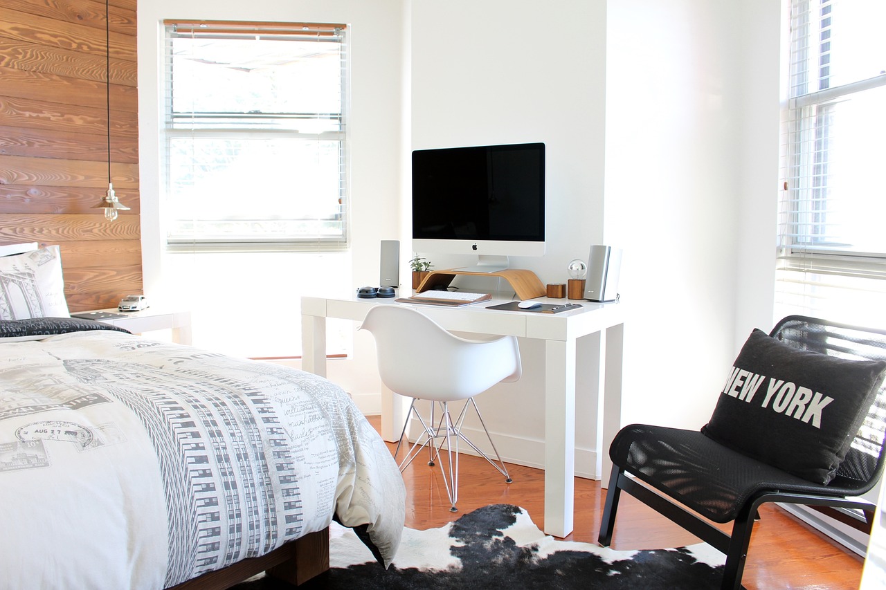 A clean and organized bedroom with a neatly made bed, minimalist decor, and sunlight pouring in through a large window, creating a cozy and inviting atmosphere.