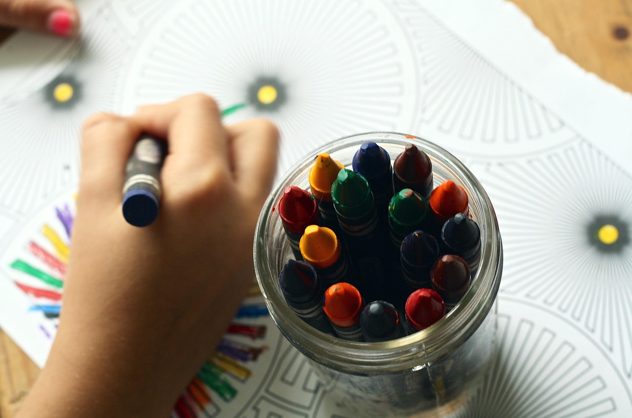 A child sitting at a table drawing with colorful crayons on paper.