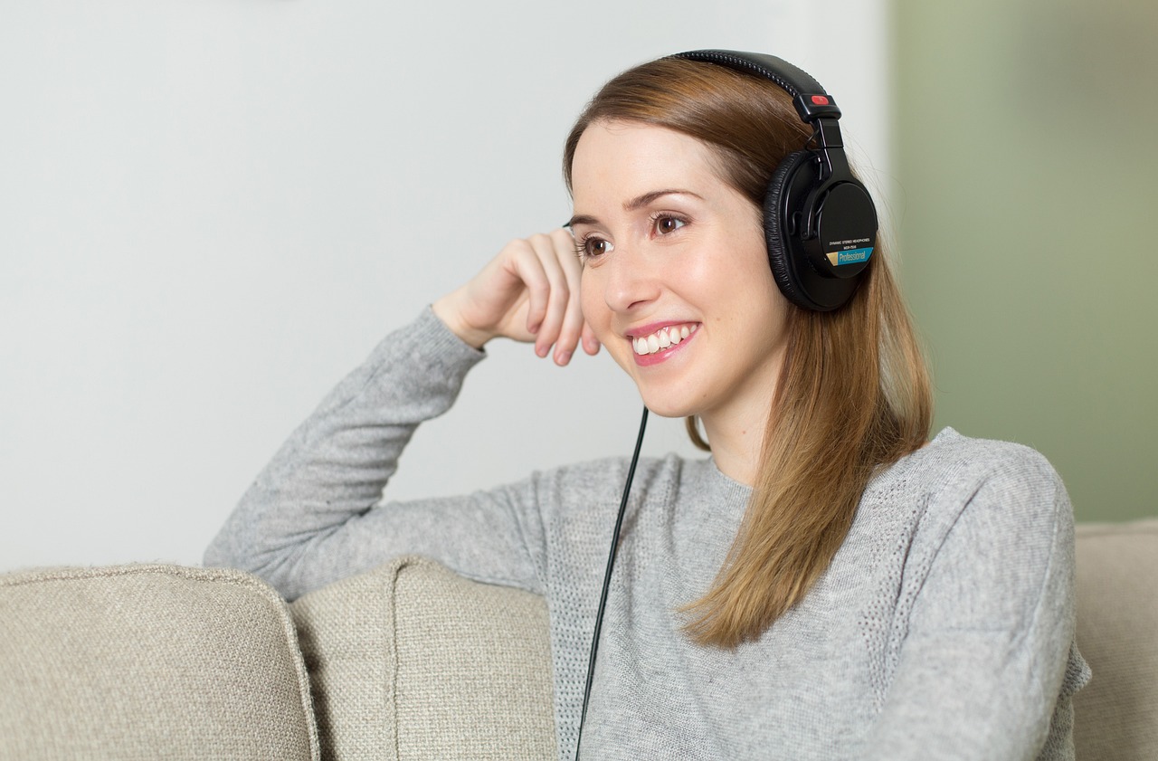 A woman relaxing on a couch, wearing headphones and enjoying music.