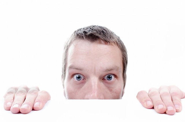 A scared man peeking over a counter, his wide eyes and hesitant posture reflecting fear and uncertainty.